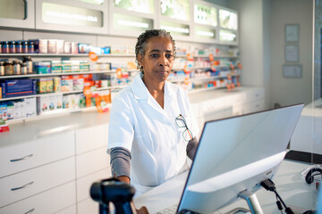 Senior female pharmacist working on computer at drugstore