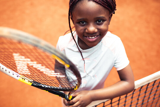Smiling little girl holding tennis racket looking at camera