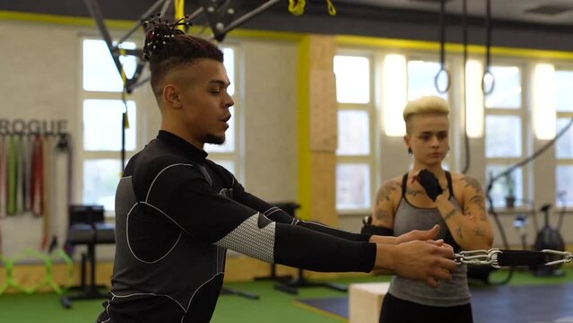 Male sport coach explaining to young woman how to training with cable crossover machine at gym. Attractive woman working out with personal coach.