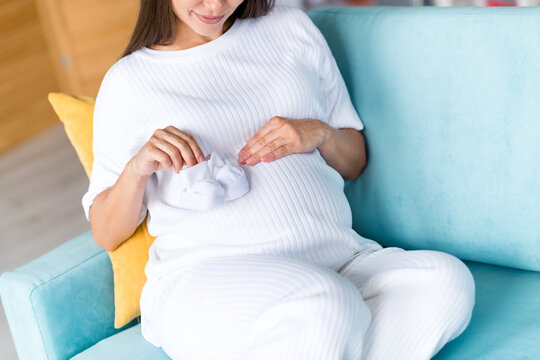 Cropped photo of adorable tender sweet dreamy mum mama pregnant girl sitting on couch showing white socks touching her big tummy