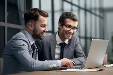 Fototapeta premium Two young businessmen sitting at workplace and working together in office