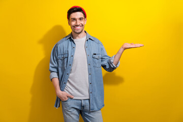 Photo of positive charming guy wear denim jacket holding arm empty space isolated yellow color background