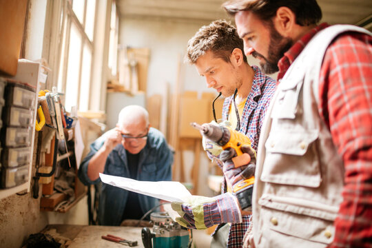 Three Men Engaged in Woodworking Project in Sunlit Workshop