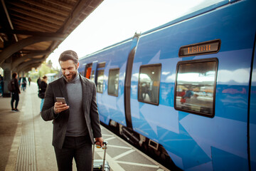 Young bearded businessman checking smartphone at train station
