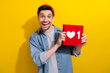 Photo of excited funky guy wear denim jacket rising positive heart like card isolated yellow color background