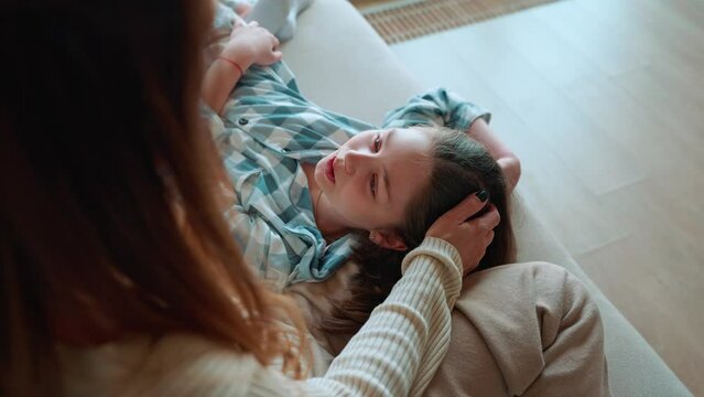 Top view of lovely mom stroking her daughters head and talking on couch at home