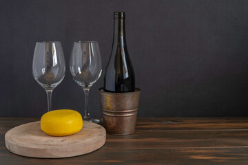 Bottle of red wine on the background of wine glasses, Gouda cheese and dark wood.