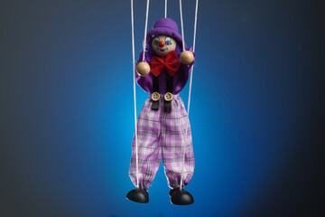 The frame features a puppet in a blue background, a marionette that hangs from strings. Someone is...