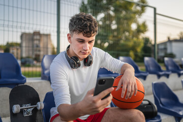 caucasian teen using mobile phone smartphone at a basketball court