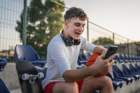 caucasian teen using mobile phone smartphone at a basketball court - Powered by Adobe