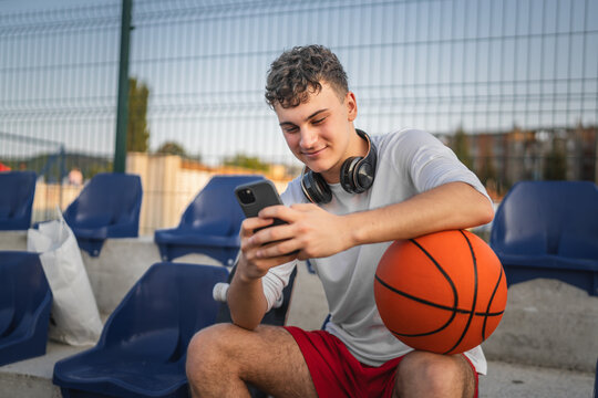 caucasian teen using mobile phone smartphone at a basketball court - Powered by Adobe