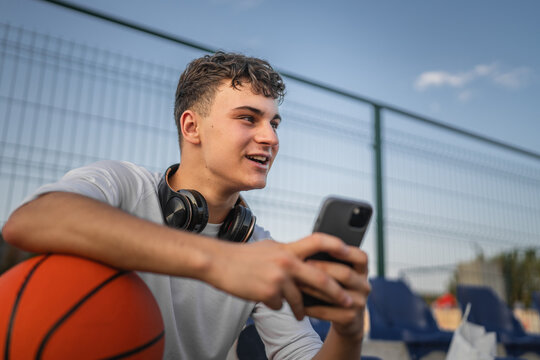 caucasian teen using mobile phone smartphone at a basketball court