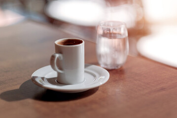Espresso coffee in a little white mug. Minimalistic approach to the concept of happy morning. Morning routine. Americano espresso in a cup with a glass of water in the background.