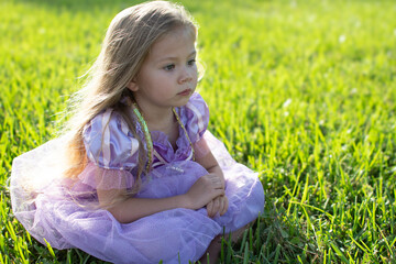 Cute Caucasian little girl sitting on a grass outdoors. Serious child. Playing outside