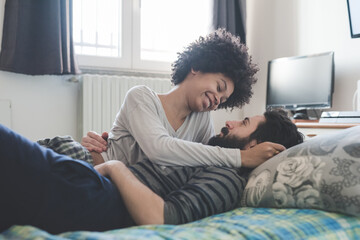 Young multiethnic couple hugging lying bed at home cuddling