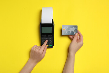 Woman using payment terminal with credit card and thermal paper for receipt on yellow background, top view - obrazy, fototapety, plakaty