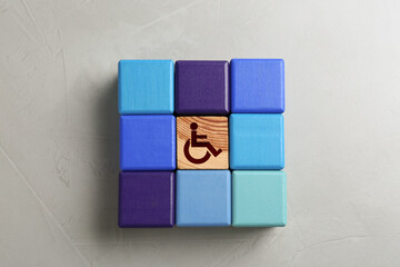 Inclusion concept. Wooden cube with international symbol of access among colorful ones on light...