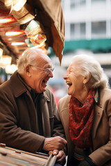 Elderly couple with white hair laughs happy. Caucasian eighty-year-old newlyweds spending good time at the market - Senior couple in coats sitting in an outdoor shop.