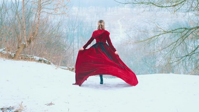 Fantasy happy woman running on top of mountain hands raised to sky, old style red fabric flies train dress waving in wind. girl enjoys winter nature fresh cold white snow fall. back rear view art 4k