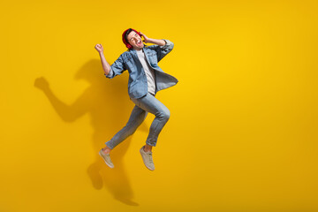 Full length photo of impressed lucky guy wear denim jacket jumping enjoying songs walking empty space isolated yellow color background