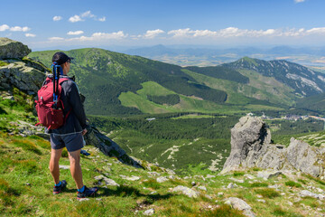 Polish Tatra Mountains, a young man in shorts and a cap with a mountain backpack stands on the...