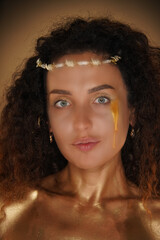 Portrait of female model in studio. Attractive girl wearing tiara and makeup covered in golden...