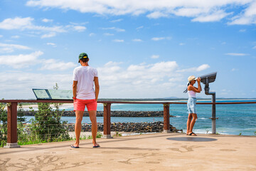 Young couple of tourists on vacation on a viewing platform by the sea, the woman looks through a...