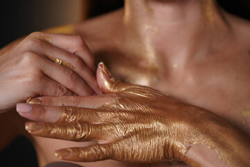 Portrait of brunette female model in studio.. Close up shot of woman hands covered in golden paint, model taking off dry gold coating from hand.