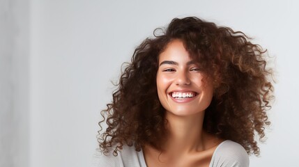 A close-up shows a young woman who is happy, winking at the camera, smiling joyfully, and standing over a white wall. - obrazy, fototapety, plakaty
