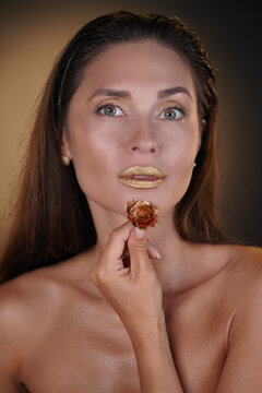 Portrait of brunette female model in studio. Attractive woman with hairstyle and bright makeup holding golden rose flower looking at the camera.