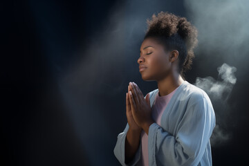 Delicate young Afro woman praying to Jesus with her eyes closed and clasped hands - profile side angle - God's rays of light shining down - Ethnic diversity and religion concept - obrazy, fototapety, plakaty