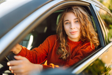 Young smiling woman driving a car drives around the city. Curly-haired woman travels by car....