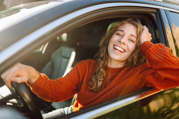 Young smiling woman driving a car drives around the city. Curly-haired woman travels by car. Lifestyle concept.