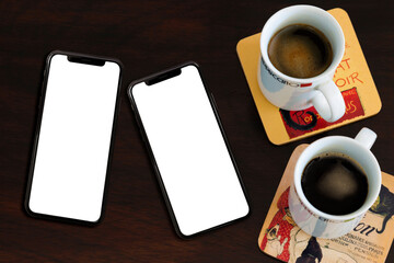 Image for mockup. Top view of two mobile phones with blank screen and next to two cups of coffee on...