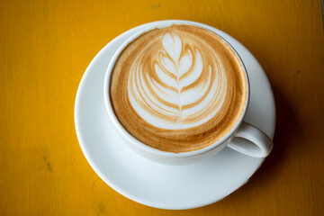 Cappuccino or latte with leaves pattern foam, coffee cleared cup closeup top view. beverage with orange wood table background by flat lay