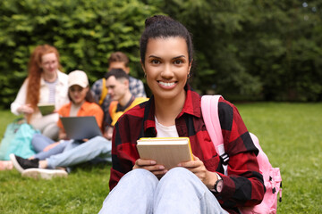 Students learning together in park. Happy woman with notebook on green grass, selective focus