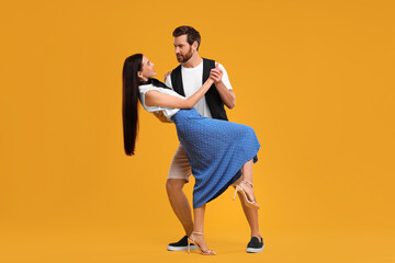 Fototapeta na wymiar Happy couple dancing together on orange background
