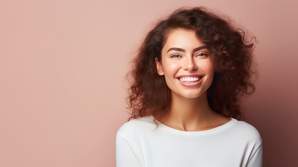 A photograph of an optimistic, lovely woman with straight hair holding her hands under her chin. She is wearing a white jumper and posing happily against a purple wall, demonstrating the