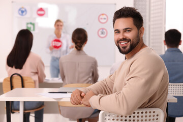 Happy man at desk in class during lesson in driving school