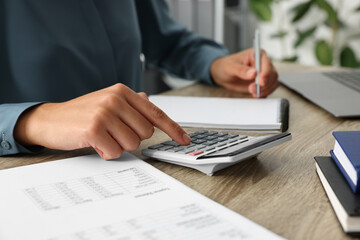 Woman using calculator while taking notes at wooden table, closeup