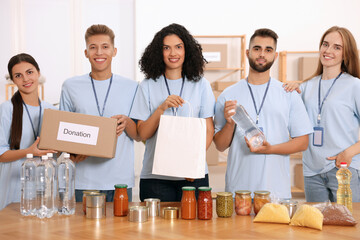 Portrait of volunteers with donation box, paper bag and food products at table in warehouse
