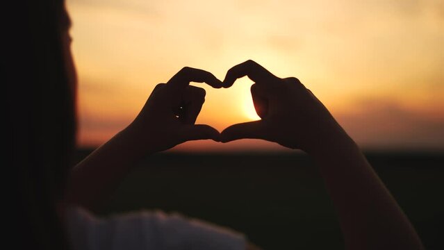 hands make a heart at sunset.happy family kid dream concept. hands in the foreground fold the figure from the fingers. a heart of fingers folded in a field lifestyle at sunset