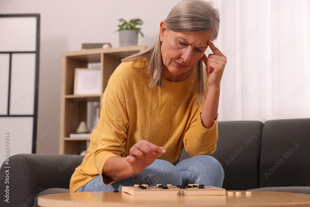 Poster Thoughtful senior woman playing checkers at home