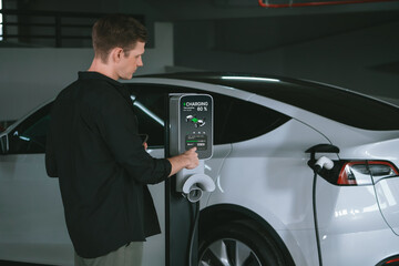 Young man travel with EV electric car to shopping center parking lot charging in downtown city...