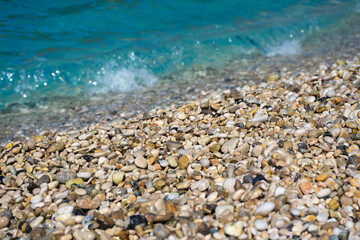 Closeup detail - small pebbles or rough sand on a beach, blurred afternoon sun lit calm sea in background