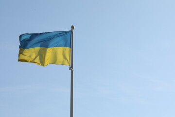 Flag of Ukraine waving on pole against blue sky. Space for text