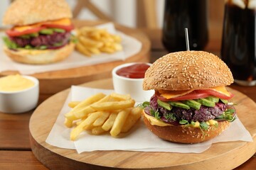 Tasty vegetarian burger served with french fries and sauce on wooden table