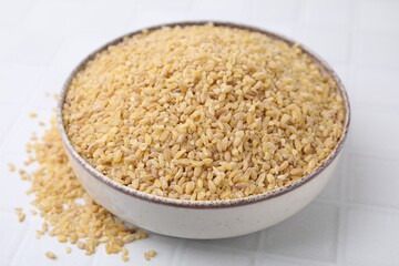 Raw bulgur in bowl on white table, closeup