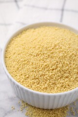 Raw couscous in bowl on light table, closeup