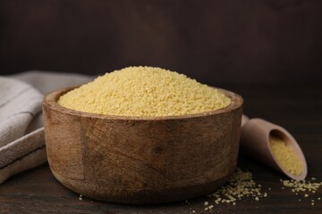 Raw couscous in bowl on wooden table, closeup